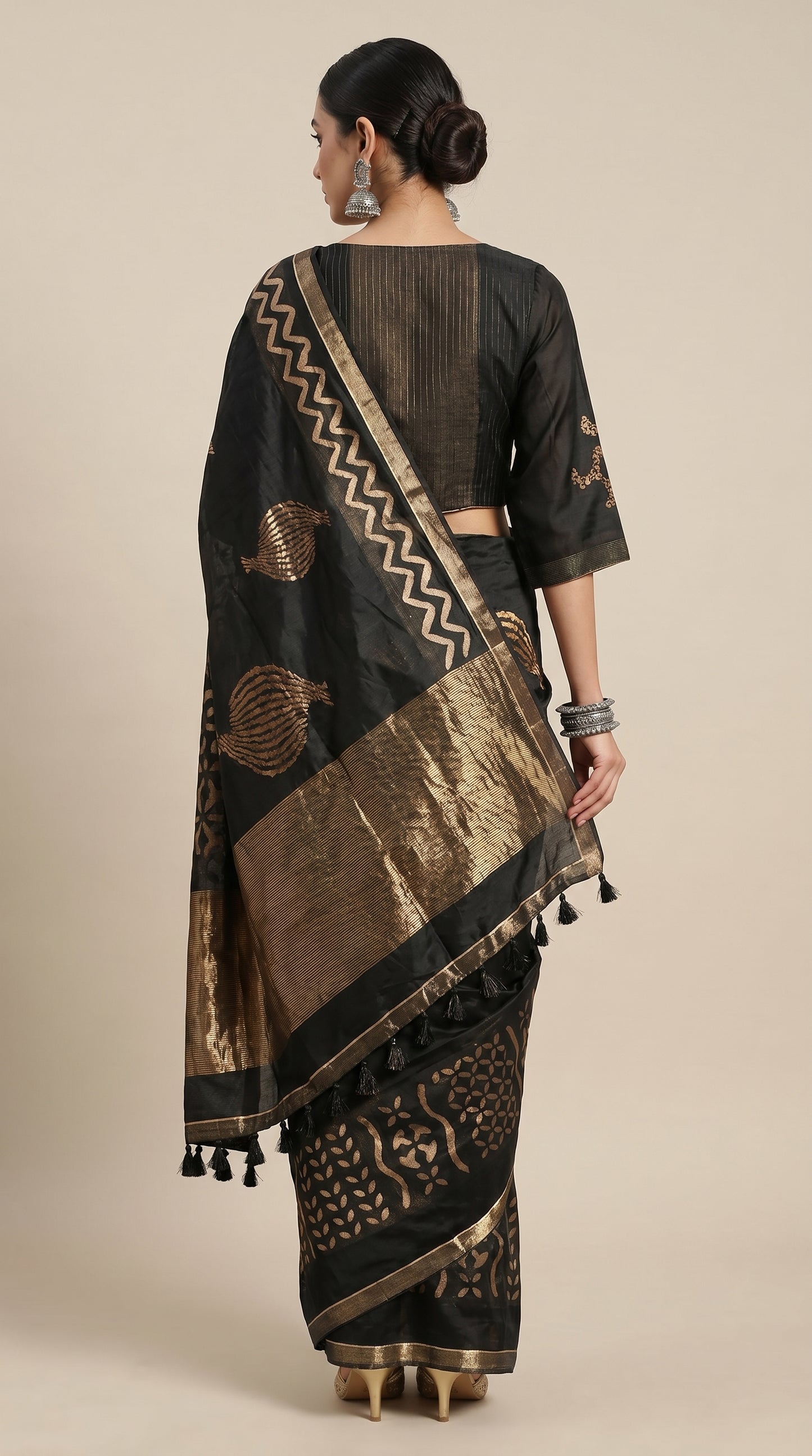 Woman wearing a black and gold saree with intricate patterns on a beige background