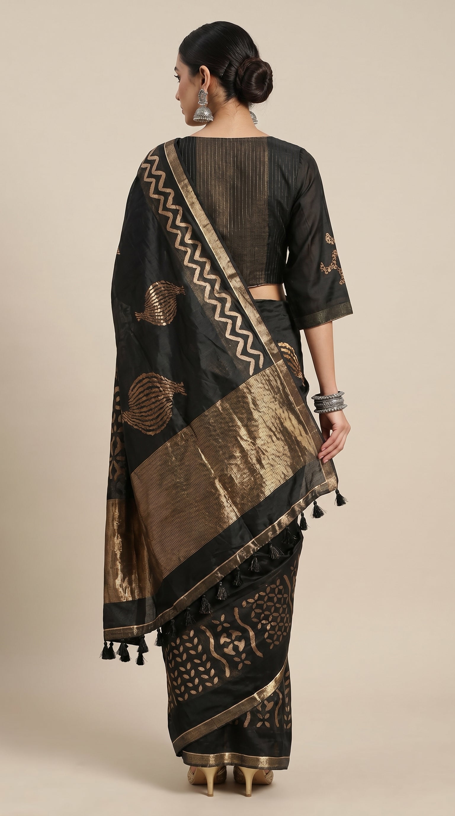 Woman wearing a black and gold saree with intricate patterns on a beige background