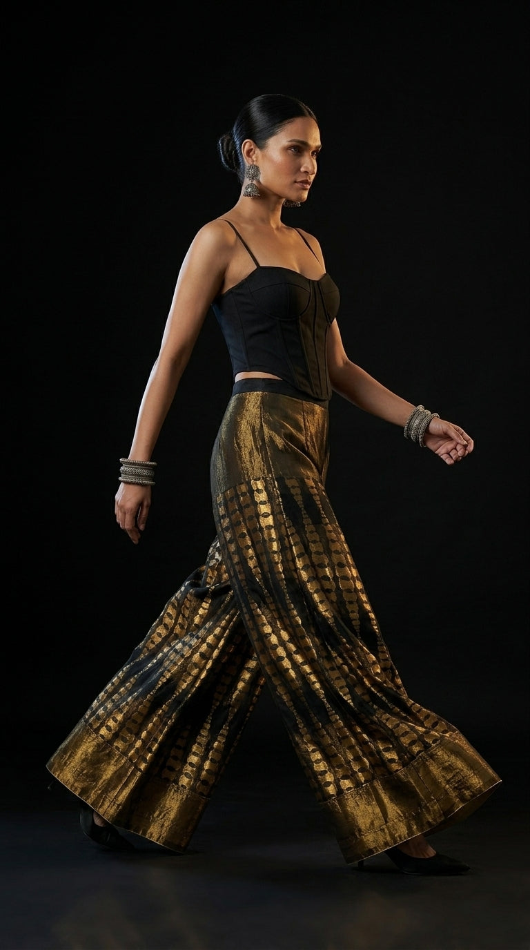 Woman wearing a black top and gold patterned plazzo on a black background