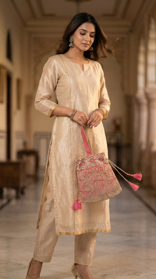 Woman in a beige traditional outfit holding a pink handbag in an indoor setting