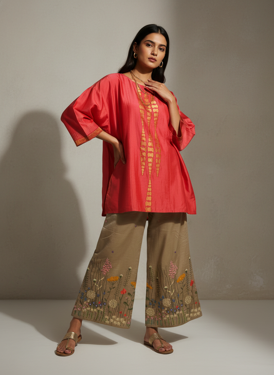 Woman wearing a pink top and beige pants with floral embroidery against a neutral background