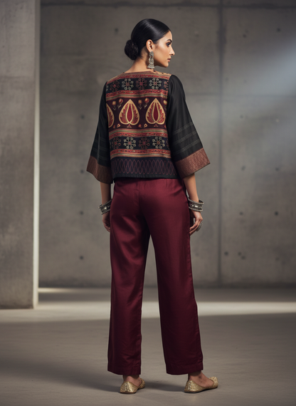Woman wearing a traditional with a patterned jacket and maroon pants against a neutral background