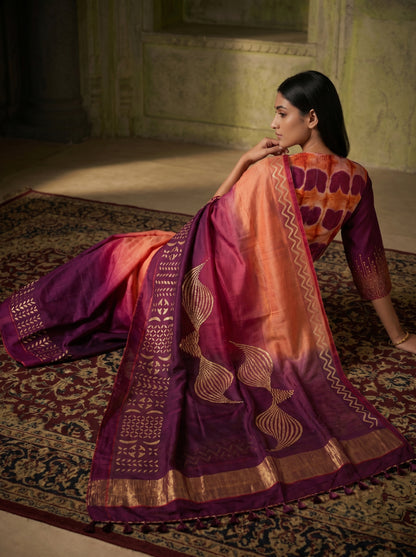 Woman wearing a traditional saree with intricate patterns in a dimly lit room.