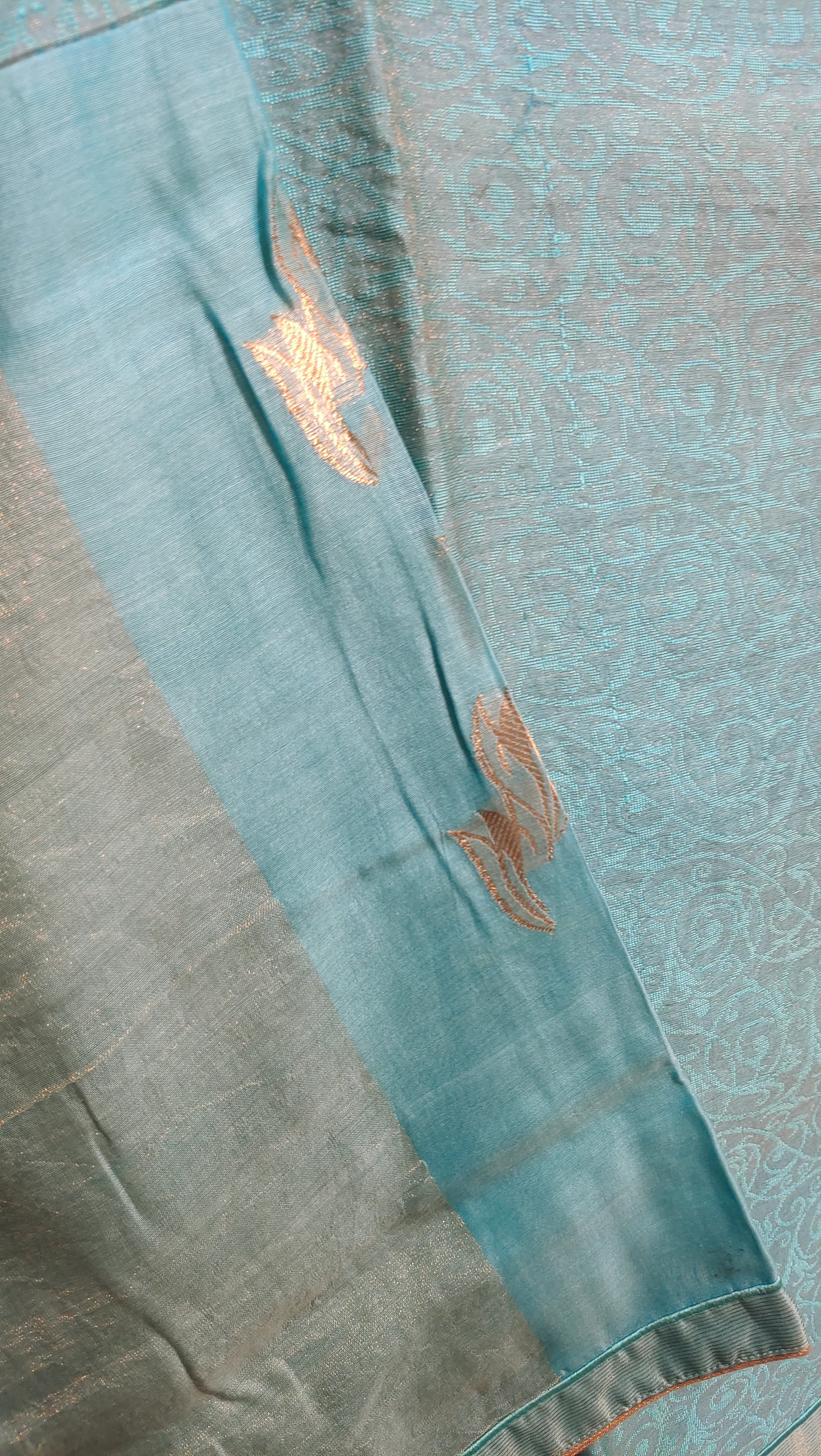 Teal fabric with gold embroidery on a textured background