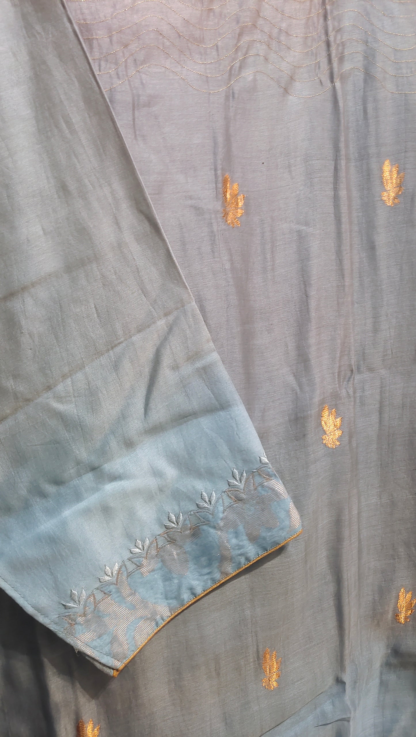 Light blue fabric gold embroidery on a wooden surface