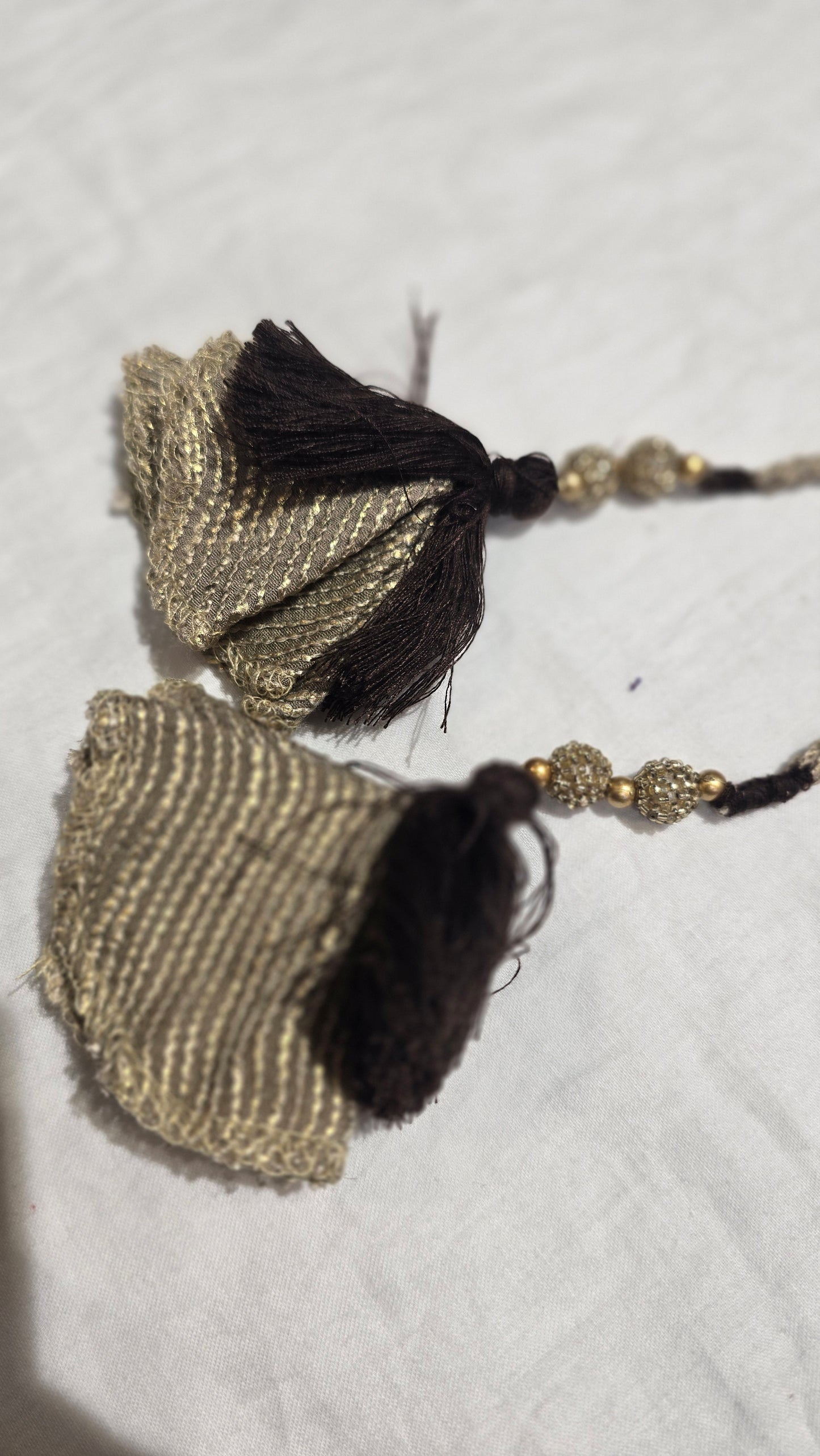 Pair of gold and black tassel earrings on a textured white surface